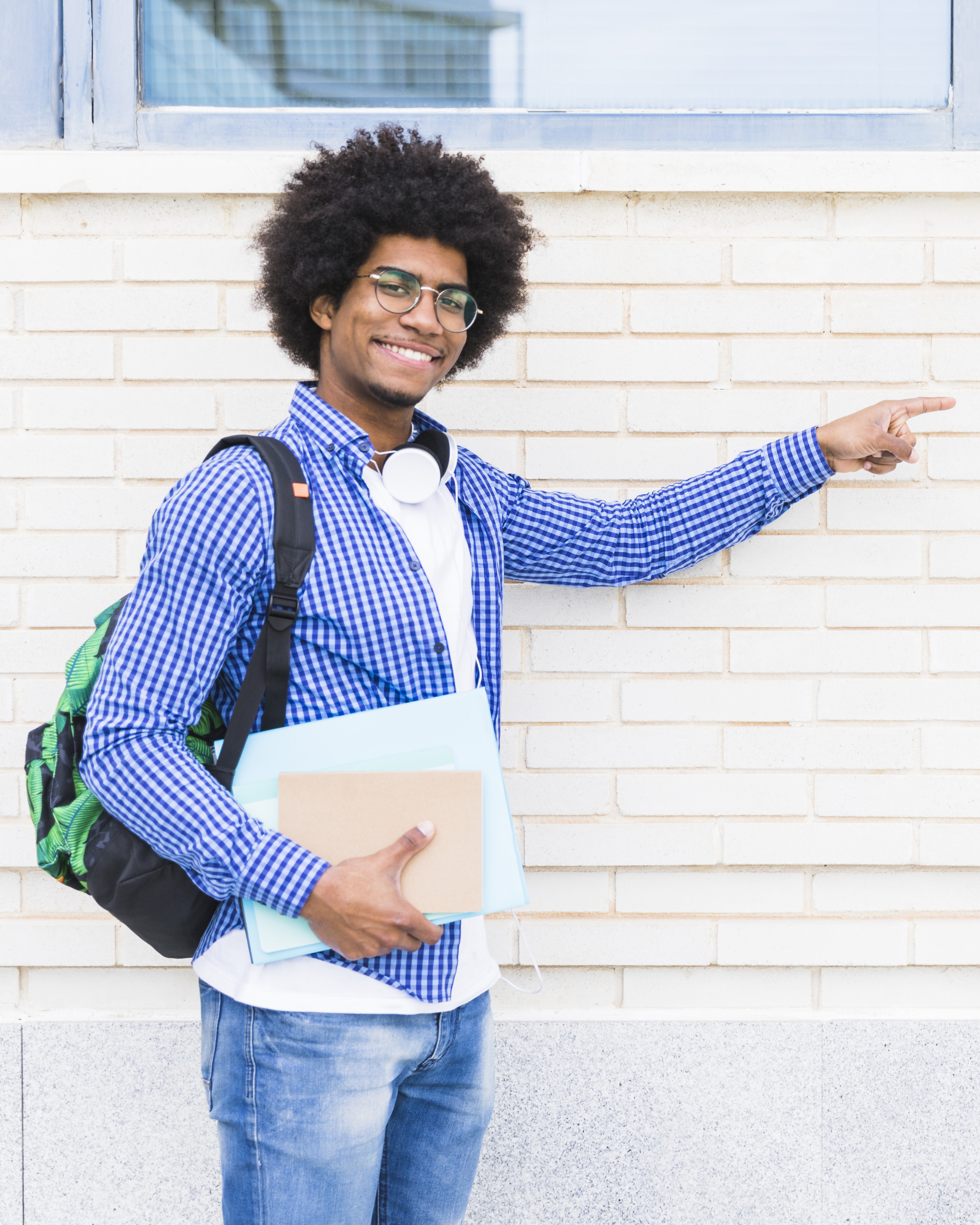 portrait-african-smiling-male-student-holding-books-hand-pointing-finger-white-painted-wall